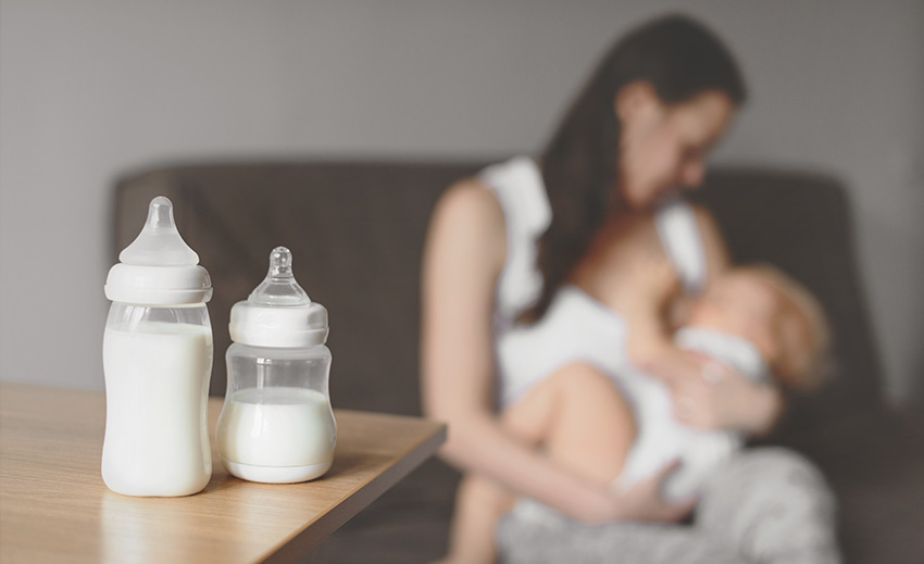 Bottles with breast milk with a woman breastfeeding a baby in the background.