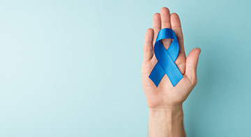 A hand holding a blue ribbon for Prostate Awareness