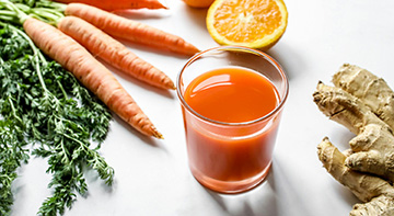 A glass of orange liquid surriounded by carrots, oranges and ginger.